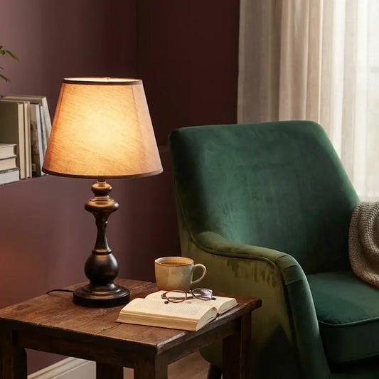 Green armchair with a wooden side table featuring a lamp, books, and a cup.
